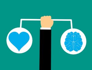 Hand holding a balance scale with a heart on one side representing emotions and a brain on the other side representing rational thought, symbolising the balance achieved through emotional intelligence.